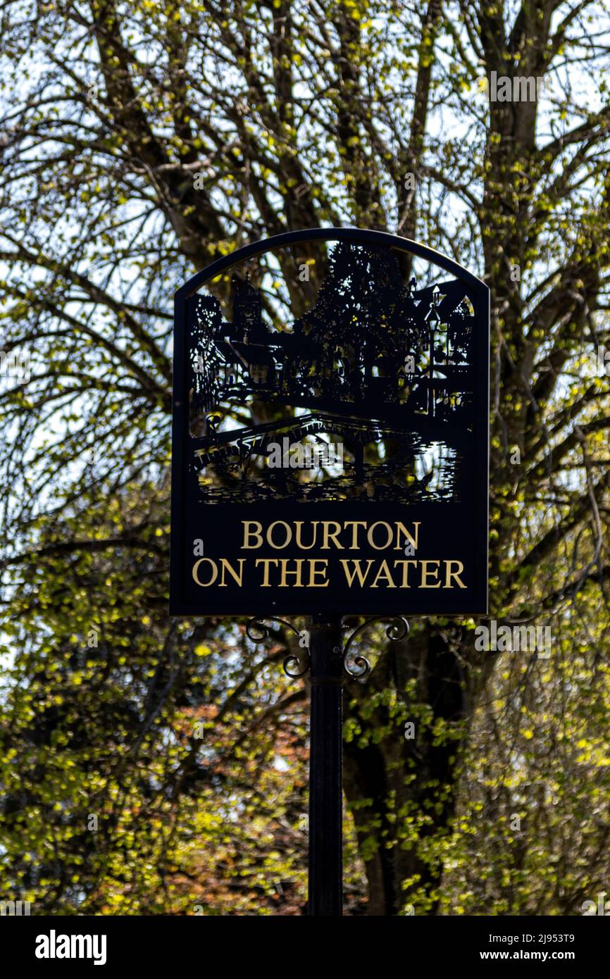 Cartello ornamentale con il nome di Bourton sull'acqua nei Cotswolds, raffigurante il fiume Windrush e il ponte basso, Gloucestershire, Inghilterra. Foto Stock