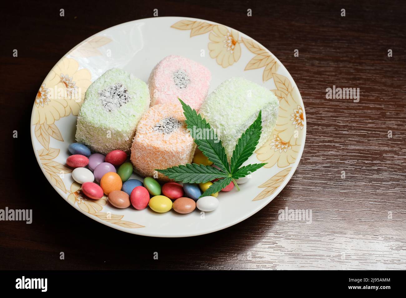 Dessert di cannabis. Delizia turca con fiocchi di cocco e confetti di caramelle colorate, vista dall'alto. Foglie di marijuana verde su fondo piatto bianco. Layout Foto Stock