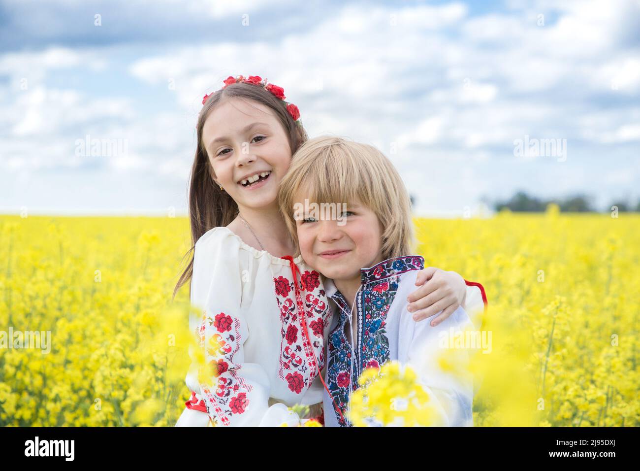 Felice ragazzo e ragazza 6-7 anni in nazionale ucraino abiti tra il fiorente campo di colza giallo. Giorno dell'indipendenza. I bambini ucraini sono chiedere Foto Stock