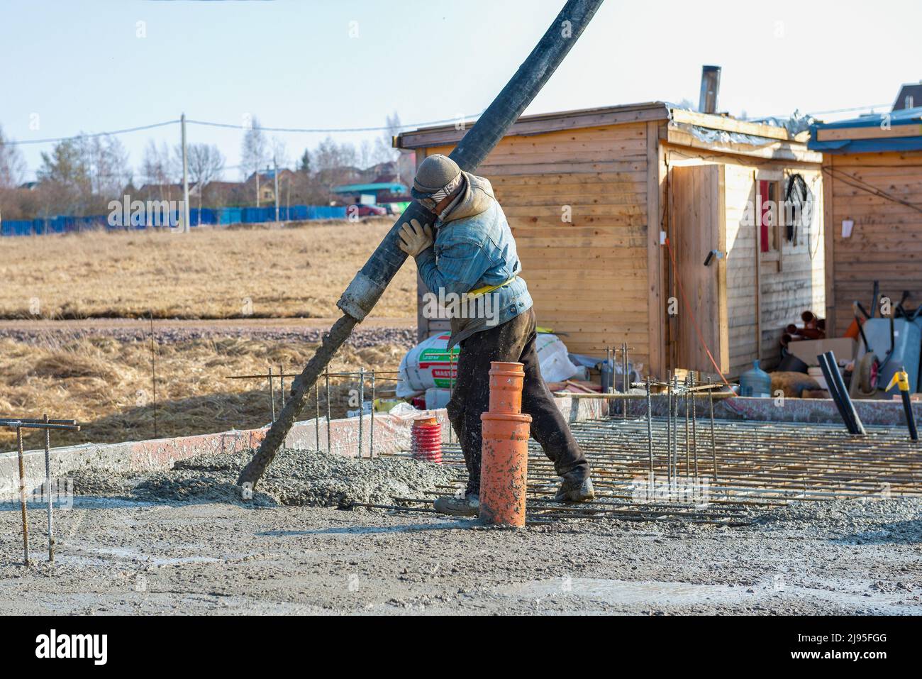 REGIONE DI LENINGRAD, RUSSIA - 28 MARZO 2021: Costruttore di lavoratori ospiti su versare la fondazione di una casa di campagna in un pomeriggio di marzo Foto Stock