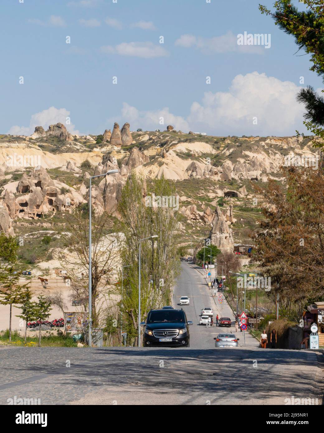 Goreme, Nevsehir, Turchia - Aprile 24 2022: Vista generale della città con traffico durante il giorno e Cappadocia formazione in pietra sullo sfondo, versione verticale. Foto Stock