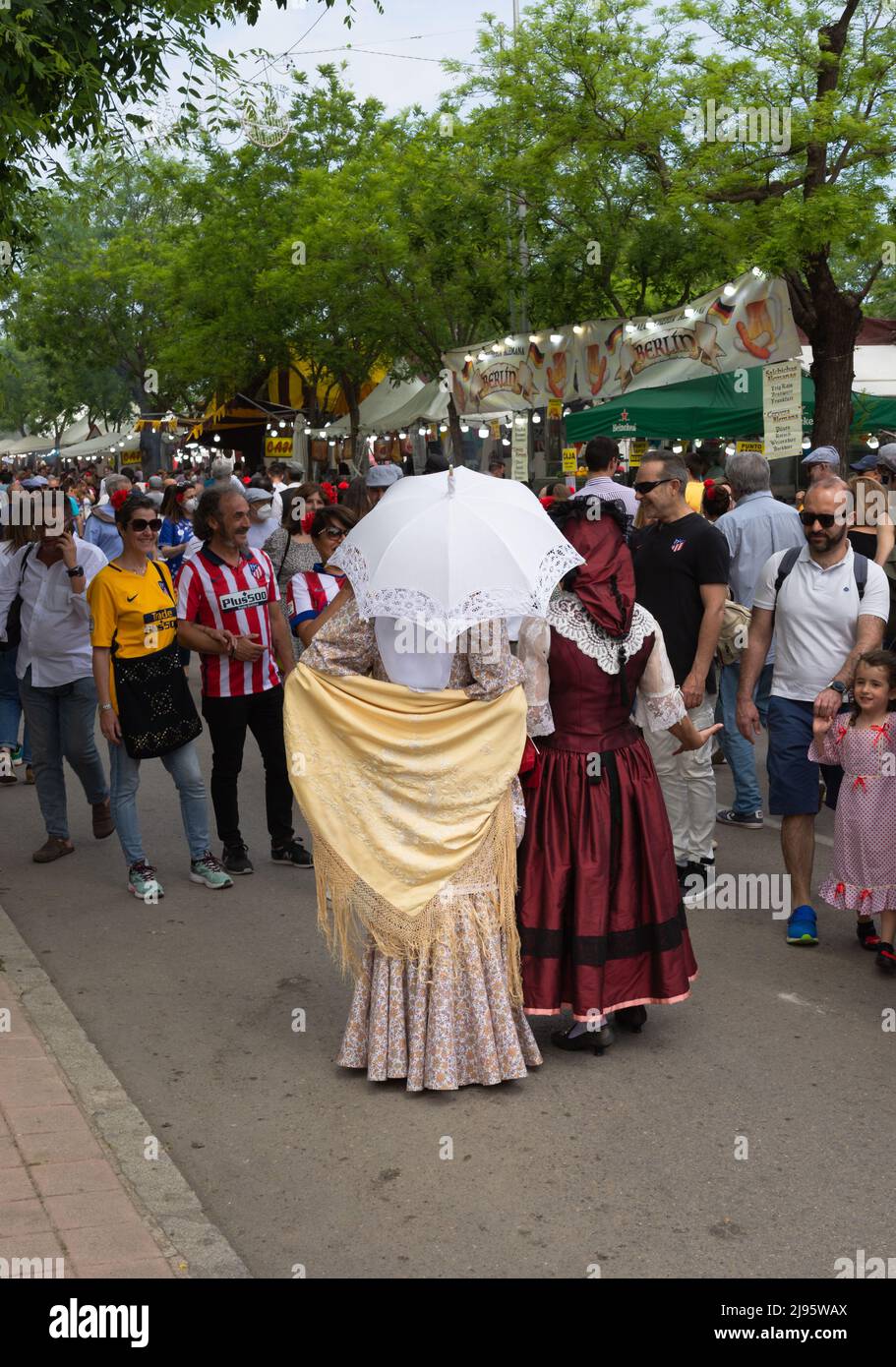 Madrid, Spagna; 15th maggio 2022: Un gruppo di persone in visita alle bancarelle della fiera di Sant'Isidro. 2 donne con le spalle girate vestite in M tradizionale Foto Stock