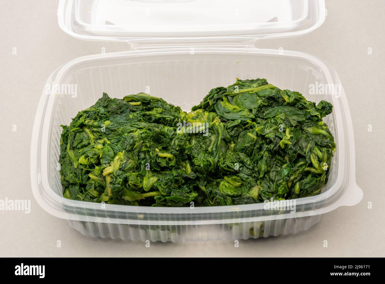 Spinaci bolliti in scatola di plastica trasparente per alimenti per refrigerazione o conservazione, su sfondo grigio chiaro Foto Stock