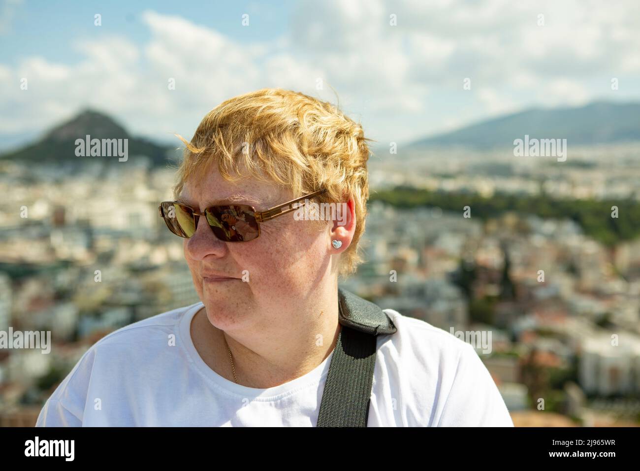 Giovane donna con occhiali da sole che guardano lontano dalla macchina fotografica con fuori fuoco skyline di Atene sullo sfondo Foto Stock