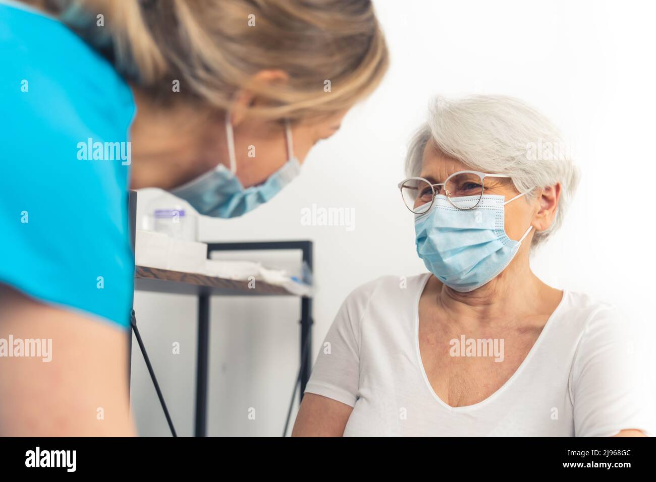 Signora caucasica vecchia amichevole rugged seduta su una sedia e sorridente ad un'operatrice di assistenza sanitaria bionda di sostegno femminile. Foto di alta qualità Foto Stock
