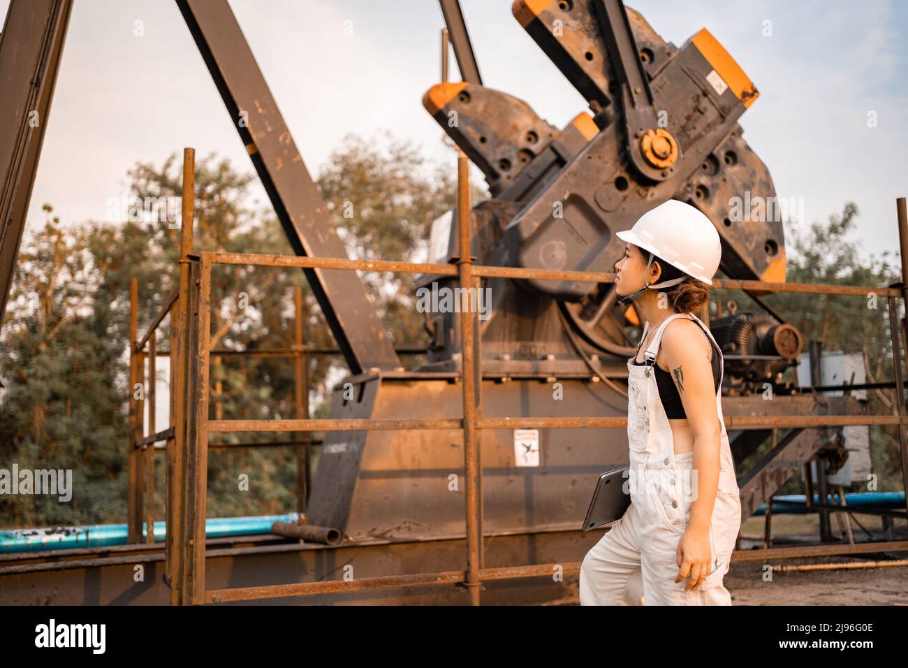 Ingegneria petrolchimica asiatica donna con casco di sicurezza in piedi nella struttura petrolifera industria petrolchimica. Foto Stock