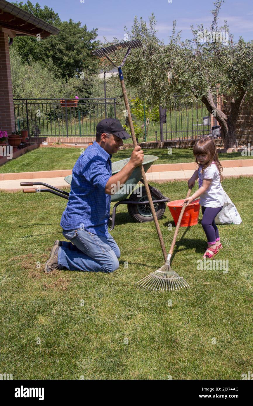 Immagine di un papà giardiniere con la figlia nel cortile mentre si aerano e raccolgono le foglie dal prato. Foto Stock