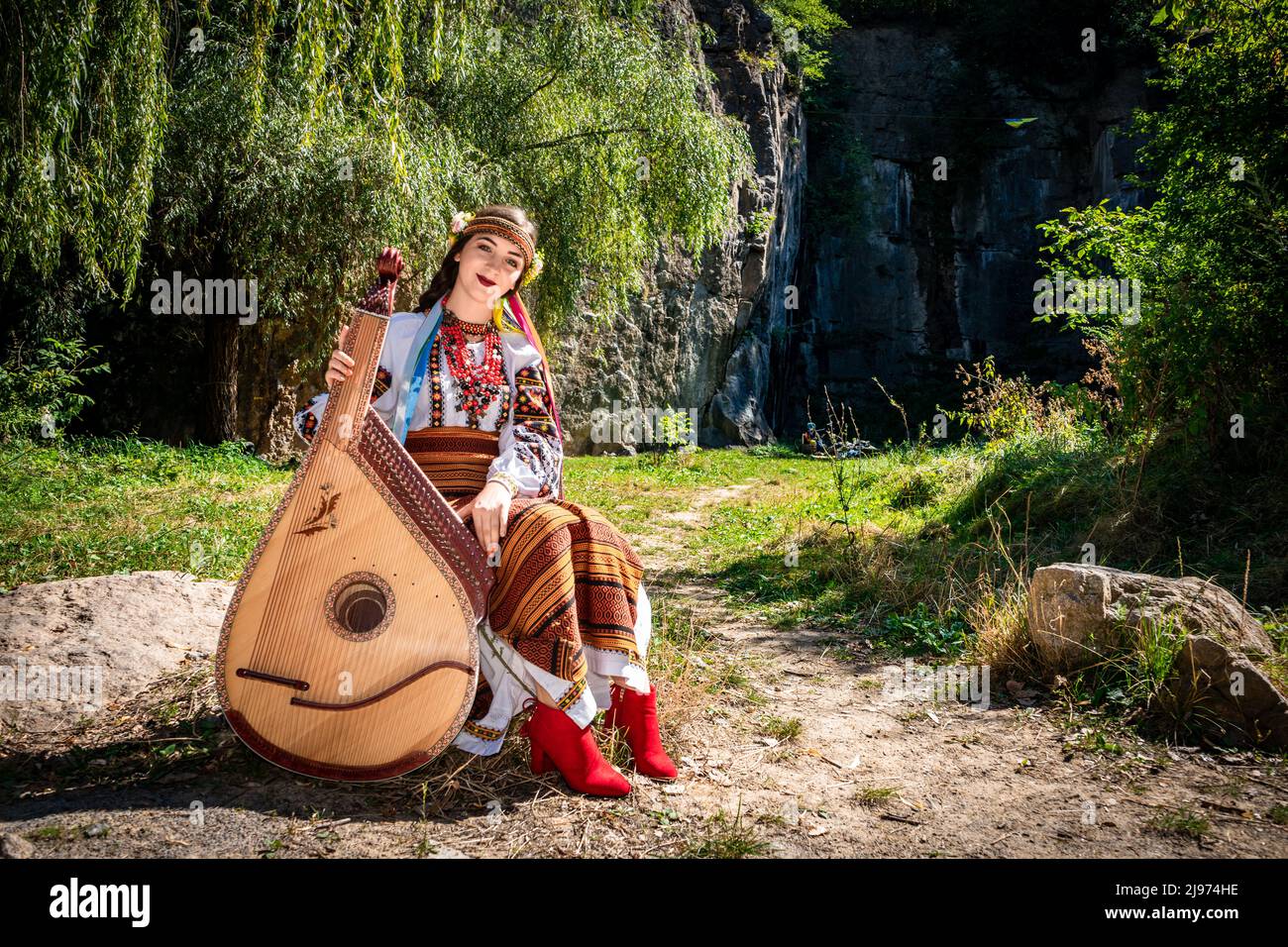 Il musicista ucraino in autentico vestito nazionale siede su una roccia. Donna Ucraina con uno strumento musicale bandura prima di eseguire musica folk. Foto Stock