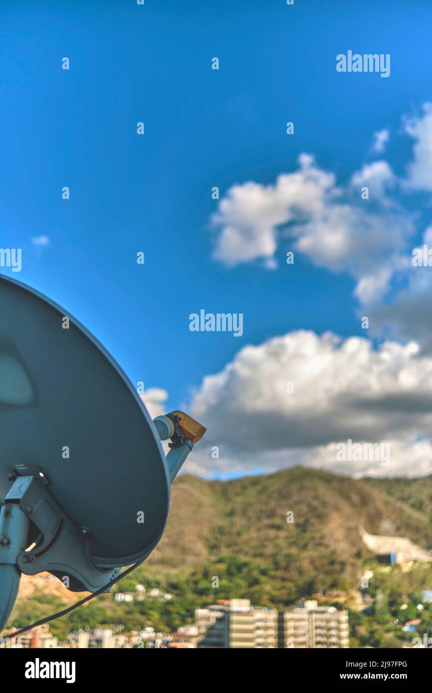 Antenna satellitare con sfondo cittadino e cielo blu, messa a fuoco selettiva Foto Stock