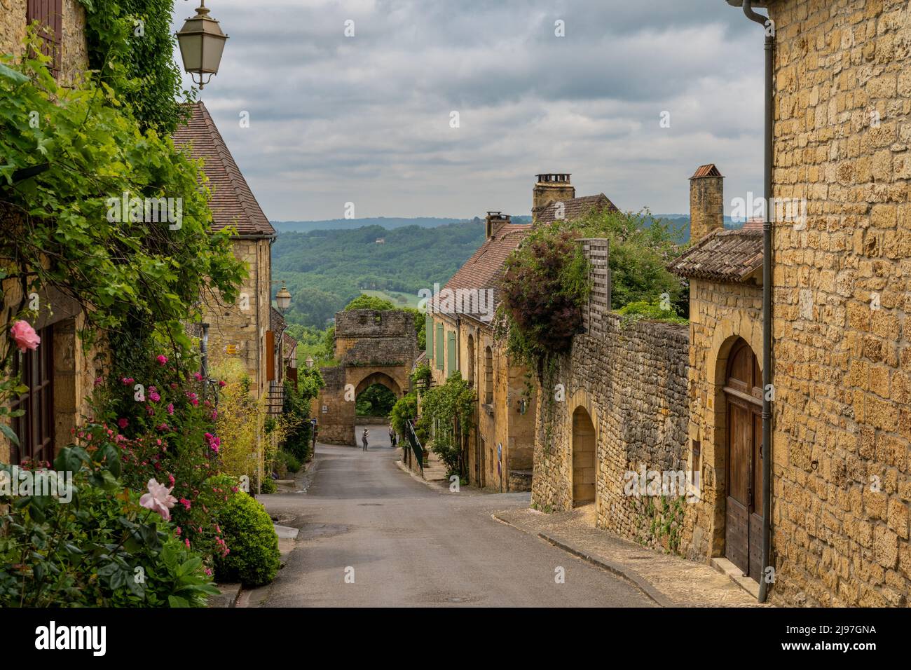 Domme, Francia - 12 maggio, 2022: Strada pittoresca con case in pietra e fiori in fiore nel villaggio storico di Domme nella valle della Dordogna Foto Stock