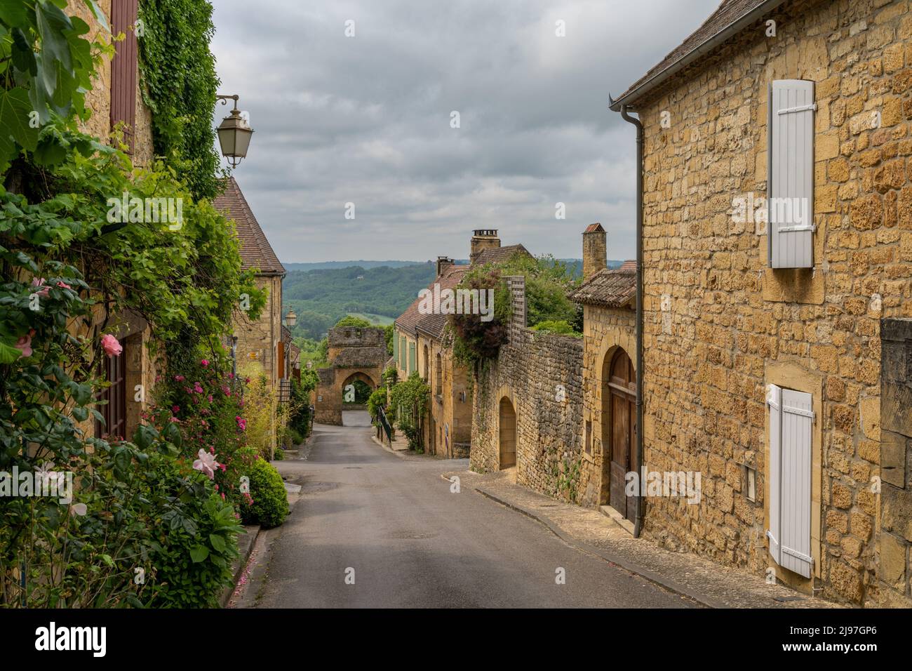 Domme, Francia - 12 maggio, 2022: Strada pittoresca con case in pietra e fiori in fiore nel villaggio storico di Domme nella valle della Dordogna Foto Stock