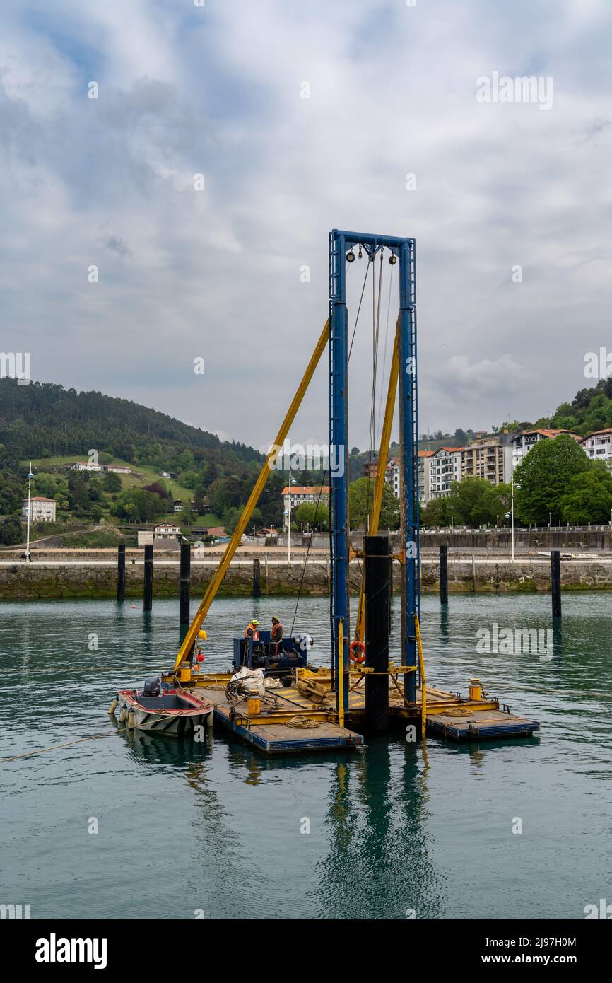 Lekeitio, Spagna - 4 maggio 2022: I lavoratori del cosntruttion montano i piloni del porto con un pilota galleggiante nel porto di Lekeitio Foto Stock