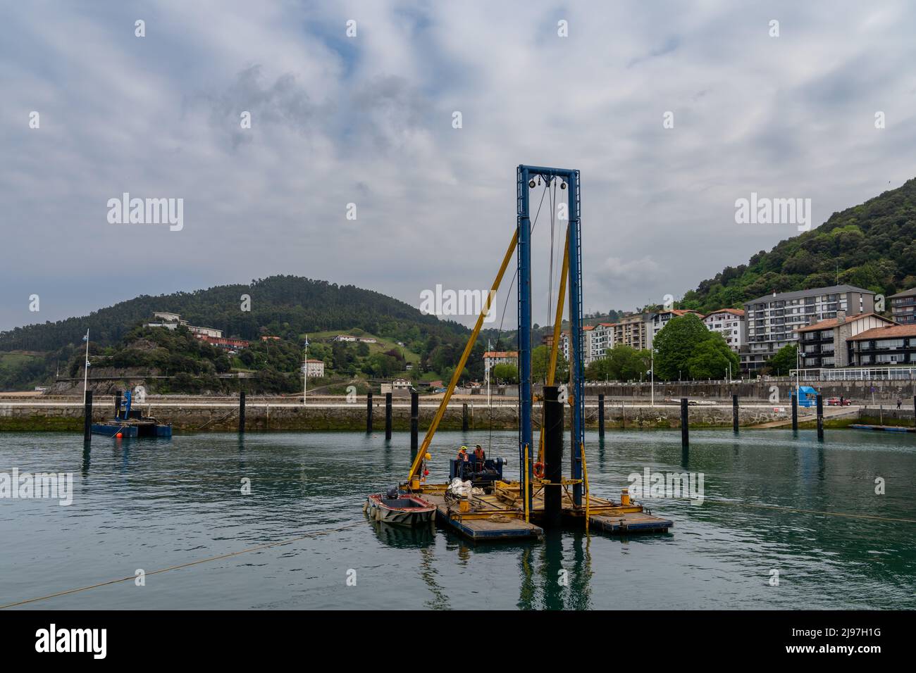 Lekeitio, Spagna - 4 maggio 2022: I lavoratori del cosntruttion montano i piloni del porto con un pilota galleggiante nel porto di Lekeitio Foto Stock