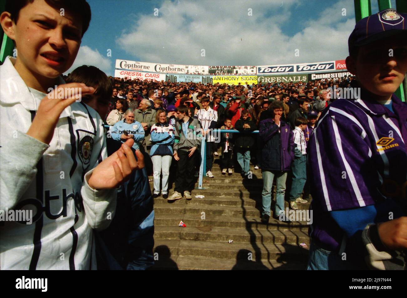 I fan si levano in piedi sulle terrazze dietro la scherma sul Kippax a Maine Road. Per la partita Manchester City contro Norwich City, 16 aprile 1994. Le recenti invasioni di campo potrebbero costringere le autorità a pensare ai metodi di prevenzione, ma sarebbe altamente improbabile che vedessimo i tifosi di calcio dietro le recinzioni. Foto Stock