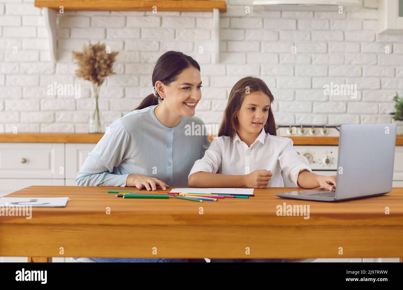 Madre e bambino seduti a tavola a casa e guardando una lezione di disegno online su un notebook Foto Stock