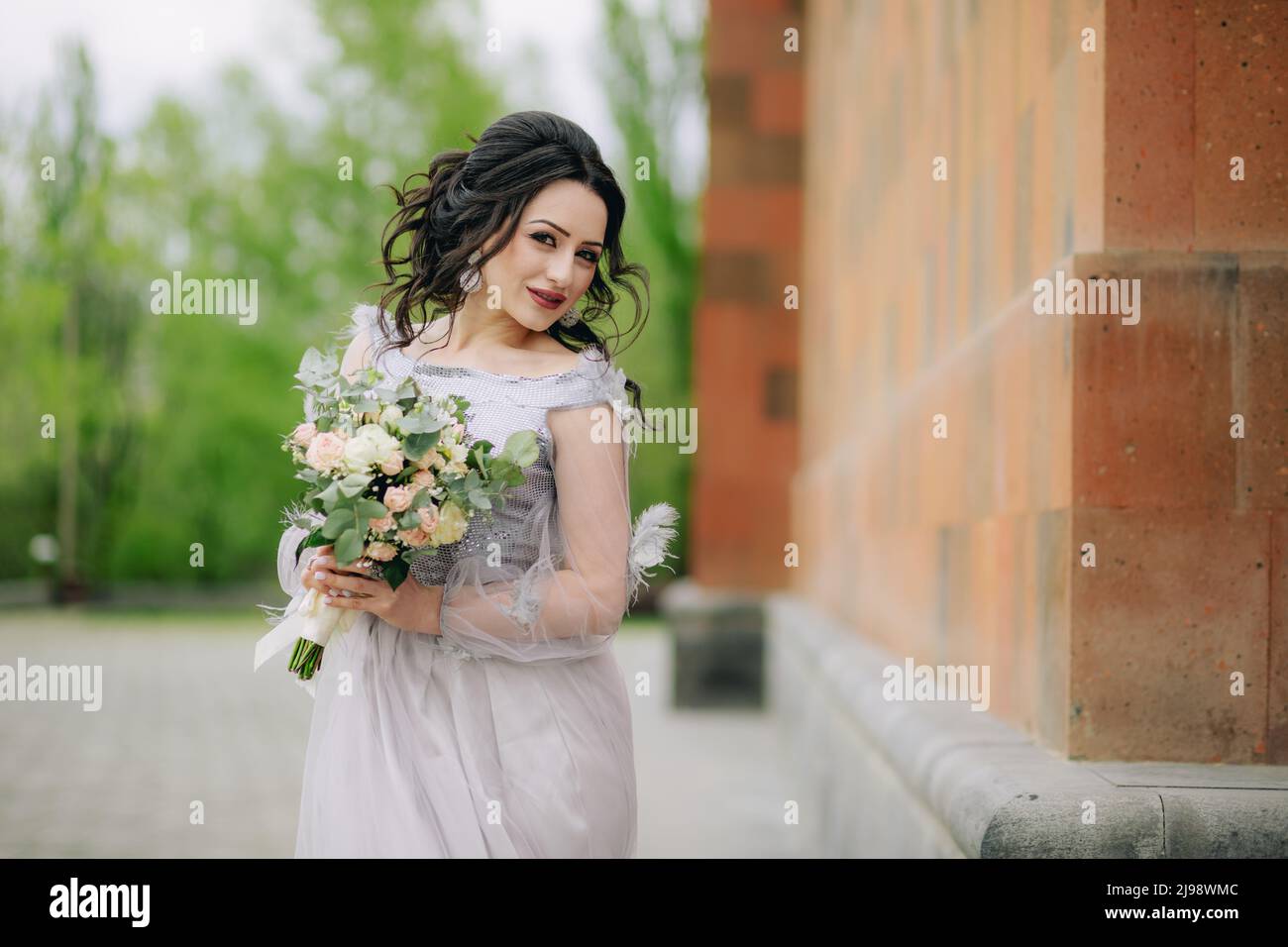 Colpo medio di bella bridesmaid con bouquet nuziale accanto alla chiesa prima della cerimonia. Foto della sirena Foto Stock