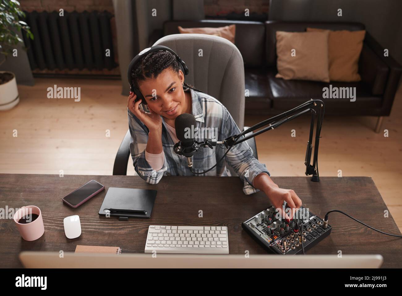 Visualizzazione orizzontale ad alto angolo di una giovane video blogger femminile seduto alla scrivania dello studio di casa controllando le impostazioni audio prima di iniziare la ripresa Foto Stock