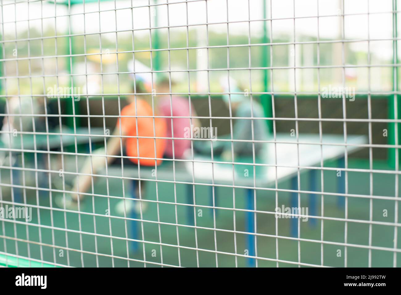 Netto sul campo sportivo. Recinzione da tavolo da tennis. Persone sfocate dietro la rete di acciaio. Foto Stock