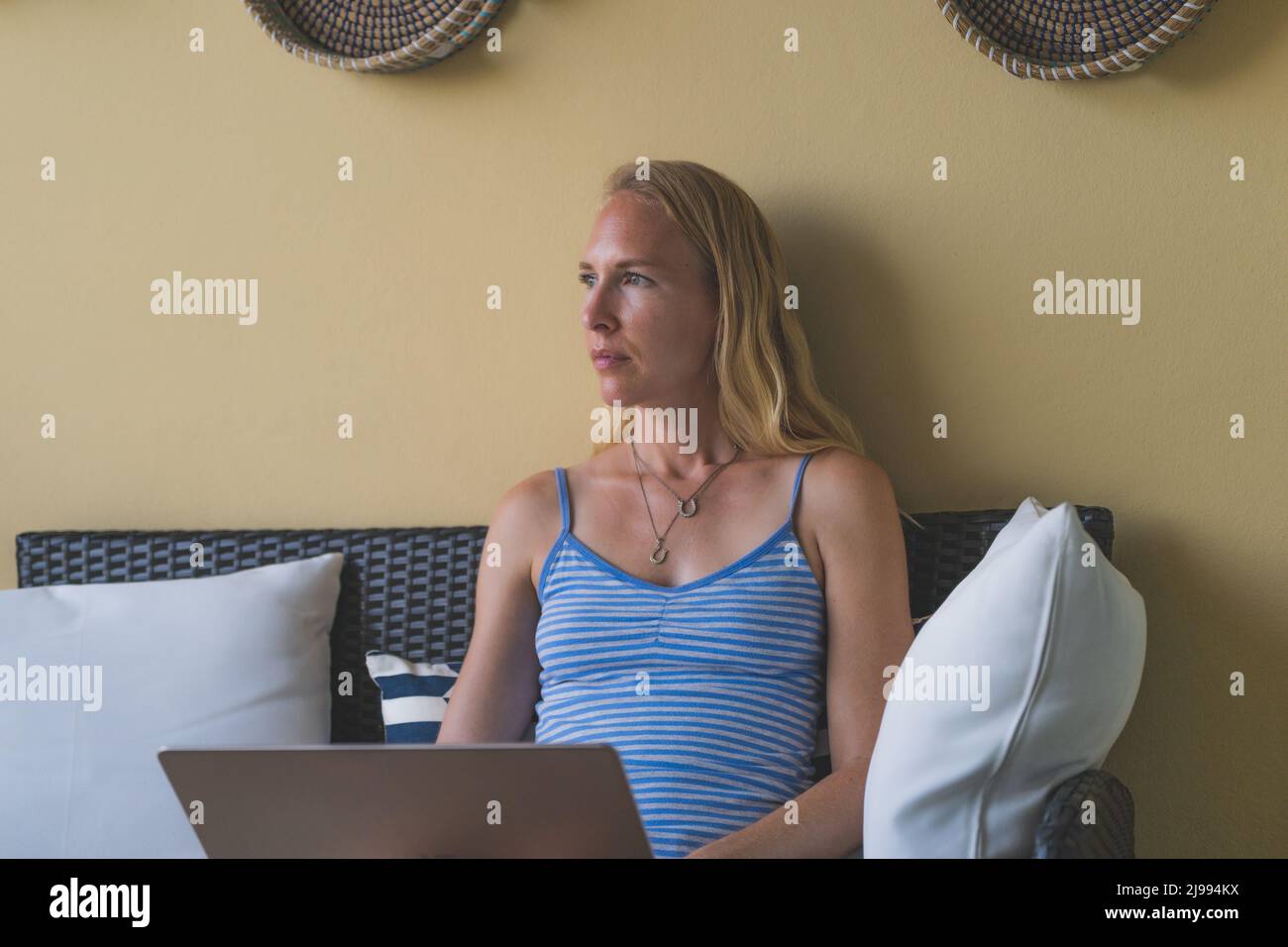 Donna che lavora su un notebook in abiti casual, seduta libera guardando lontano Foto Stock