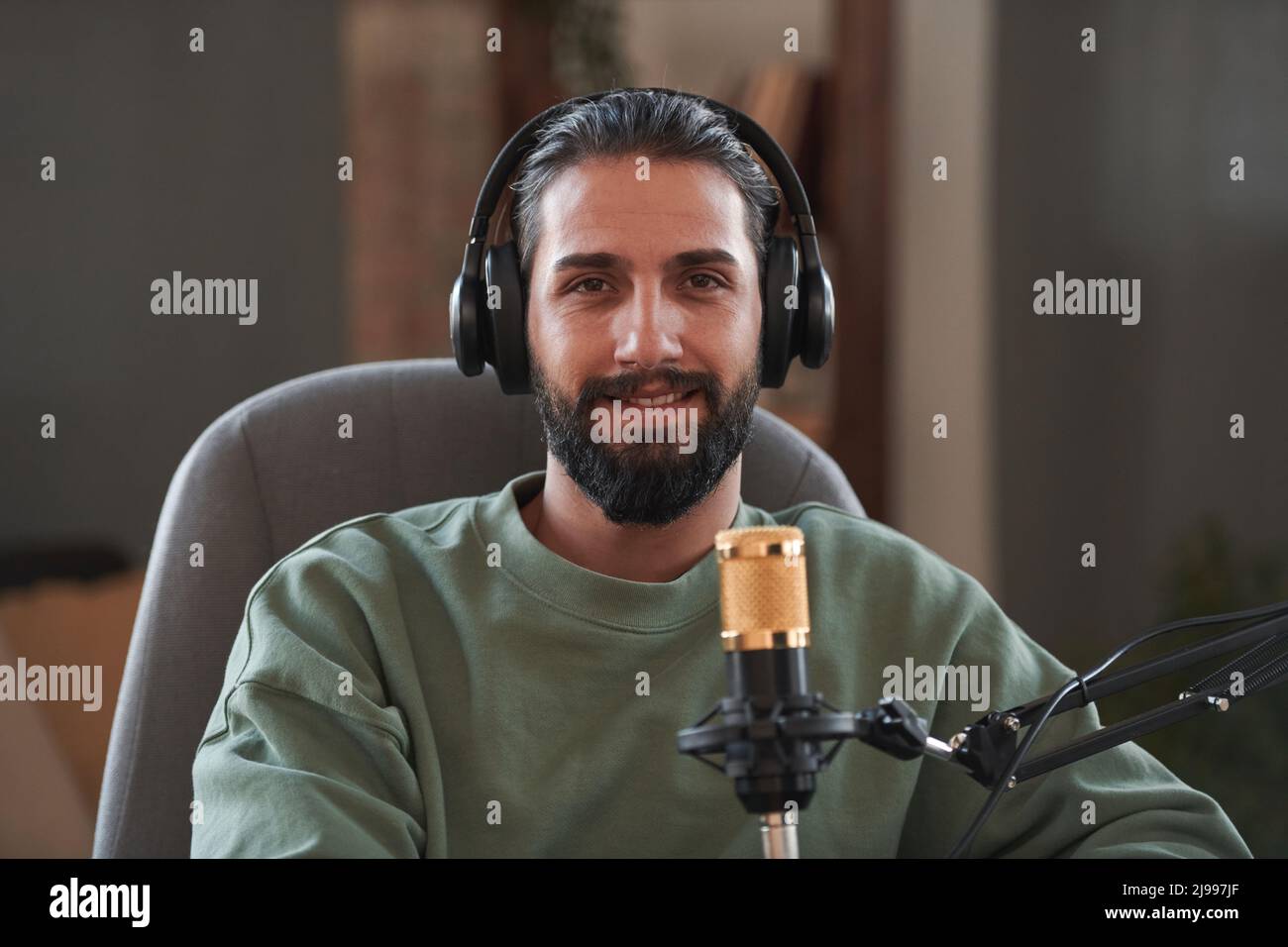 Ritratto medio di primo piano del giovane influencer mediorientale che indossa le cuffie creando contenuti per blog guardando la fotocamera Foto Stock