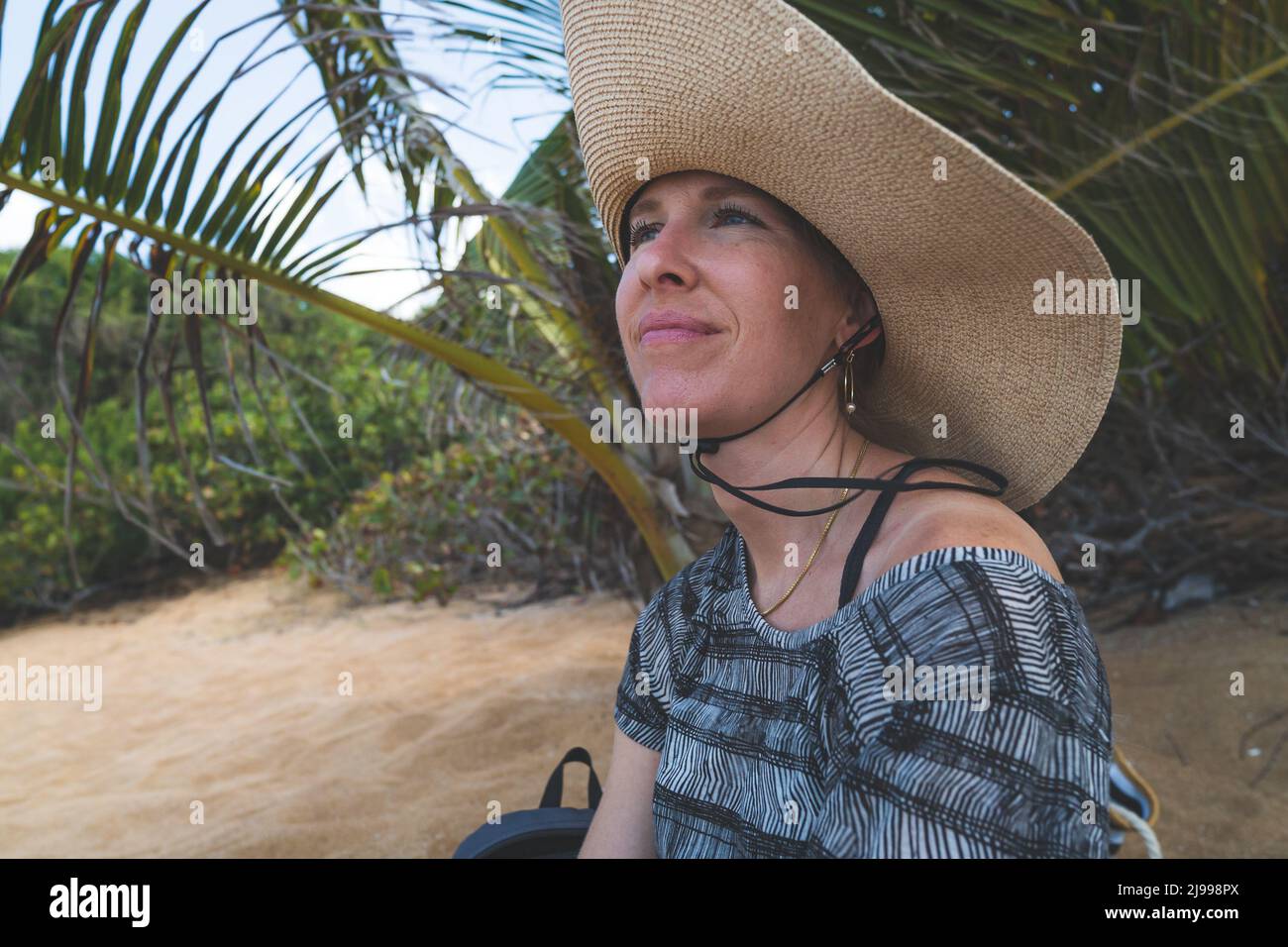 Donna sorridente in cappello di paglia seduto sulla spiaggia tropicale Foto Stock