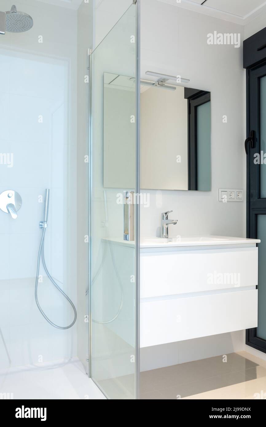 Parte di un bagno moderno. Vista su una cabina doccia in vetro e su un armadio con lavandino. Foto Stock