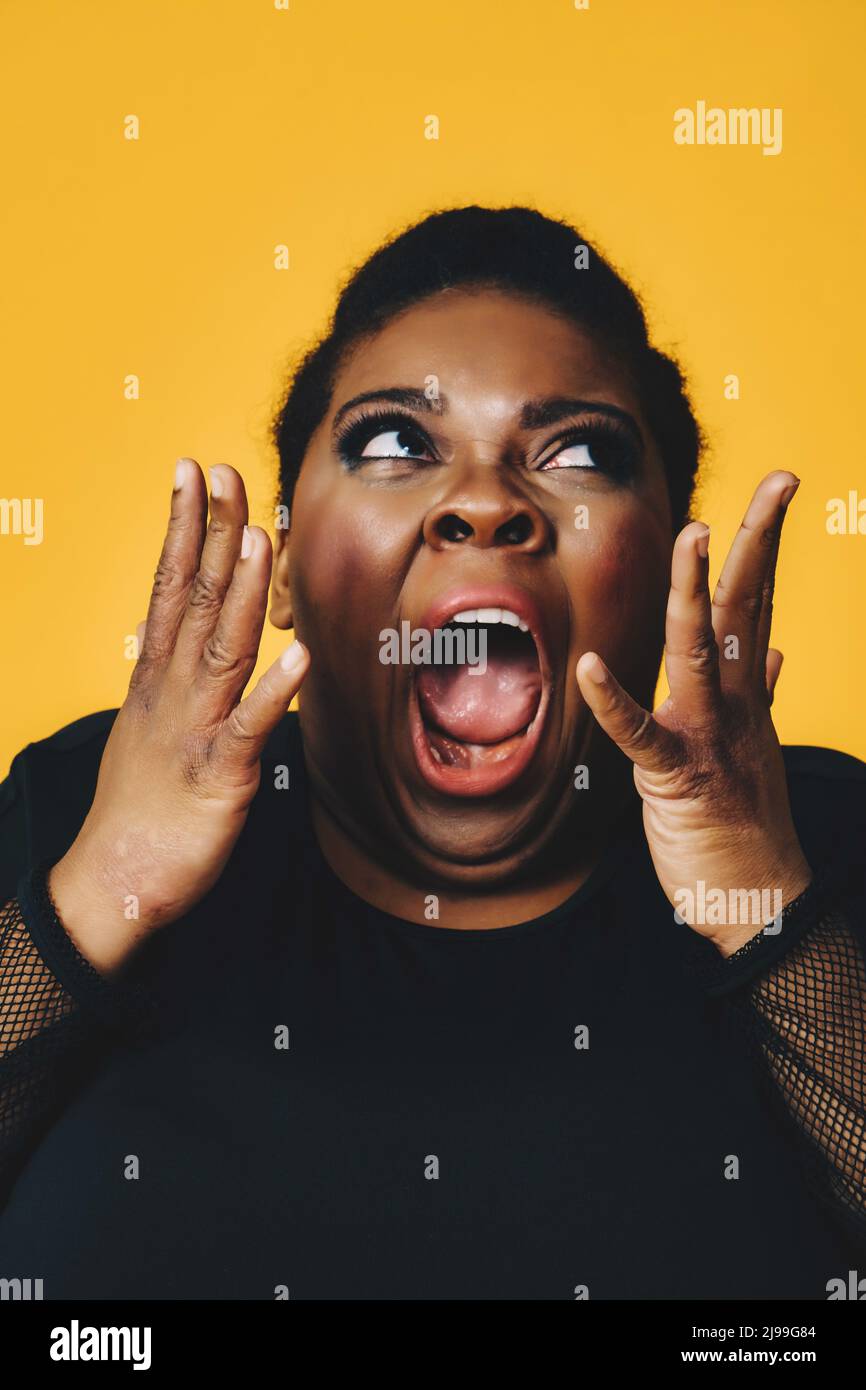ritratto closeup di una giovane donna nera adulta in shock con bocca aperta urlando su sfondo giallo studio Foto Stock