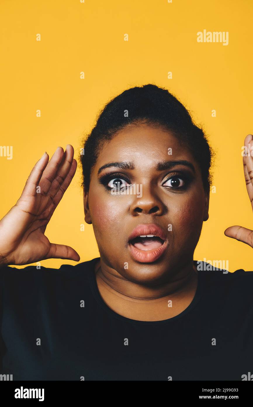 ritratto closeup di una giovane donna nera adulta in shock con bocca aperta urlando su sfondo giallo studio Foto Stock