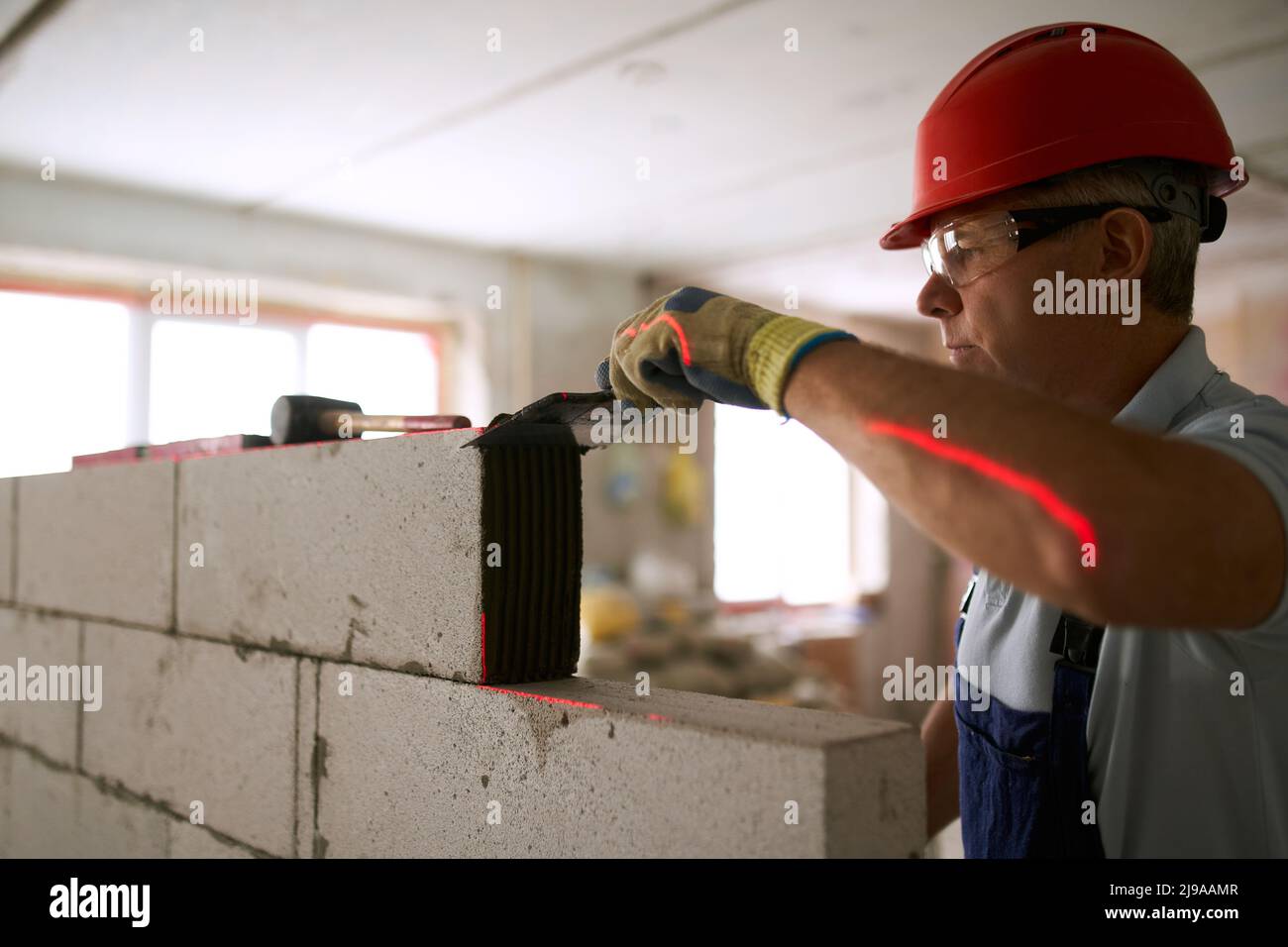 Bricklayer applica colla adesiva su blocchi di calcestruzzo cellulare autoclavati con cazzuola intagliata. L'appaltatore del lavoratore di muratura rimuove il mortaio in eccesso da Foto Stock