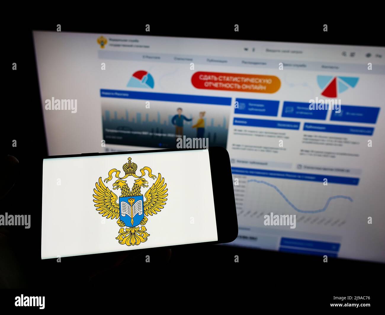 Persona che tiene uno smartphone con il logo del servizio di statistica statale federale russa (Rossat) sullo schermo di fronte al sito Web. Mettere a fuoco sul display del telefono. Foto Stock