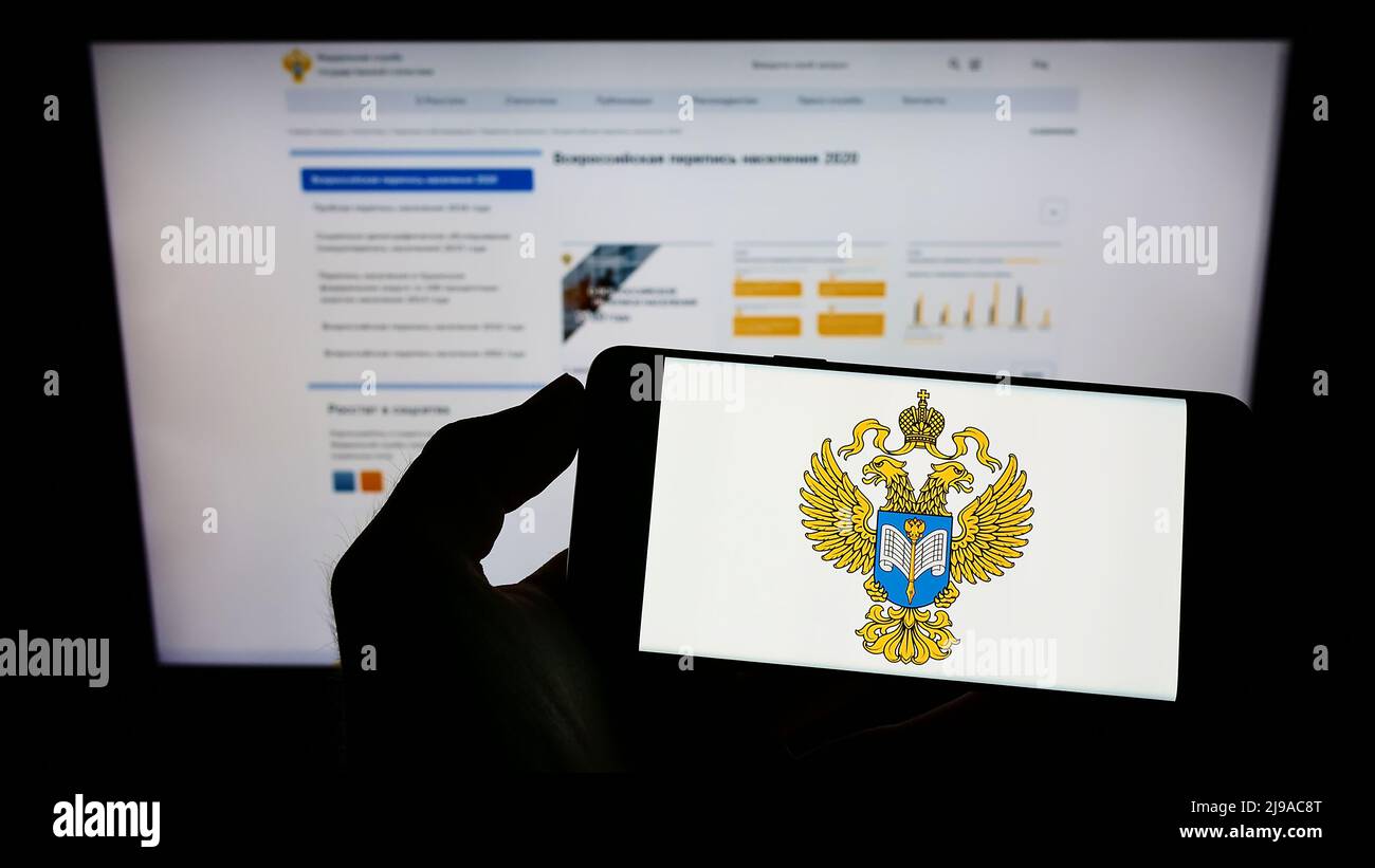 Persona che tiene il cellulare con il logo del servizio di statistica federale russa (Rossat) sullo schermo di fronte alla pagina web. Mettere a fuoco sul display del telefono. Foto Stock