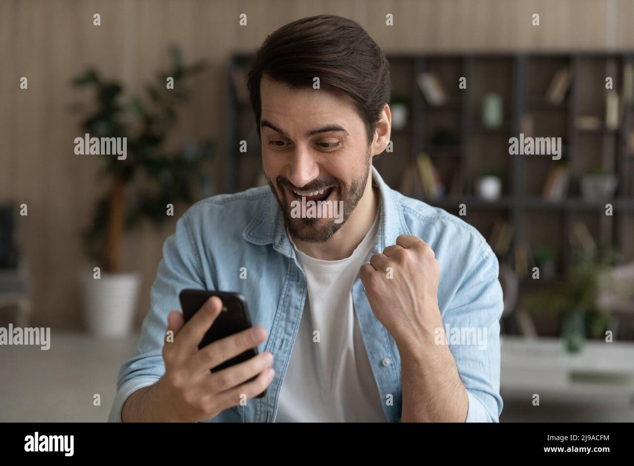 Euforica bearded maschio guardare lo schermo delle cellule ricevere in linea presente Foto Stock