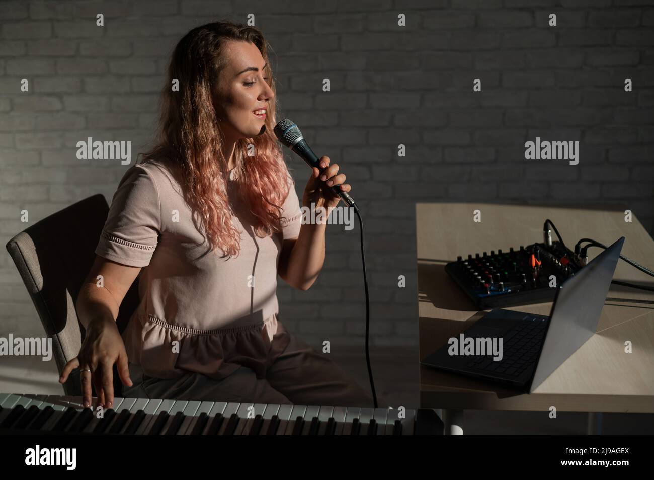 Una giovane donna europea canta in un microfono e accompagna un pianoforte elettronico. La ragazza spara un video blog. Lezione vocale remota. Una femmina Foto Stock