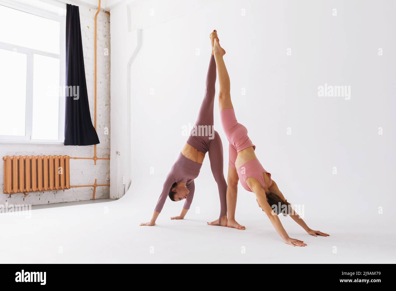 Due praticanti di yoga femminile che fanno una variante di Adho Mukha Svanasana, rivolto verso il basso cane posa con una gamba in su, stanno addestrando nello studio Foto Stock