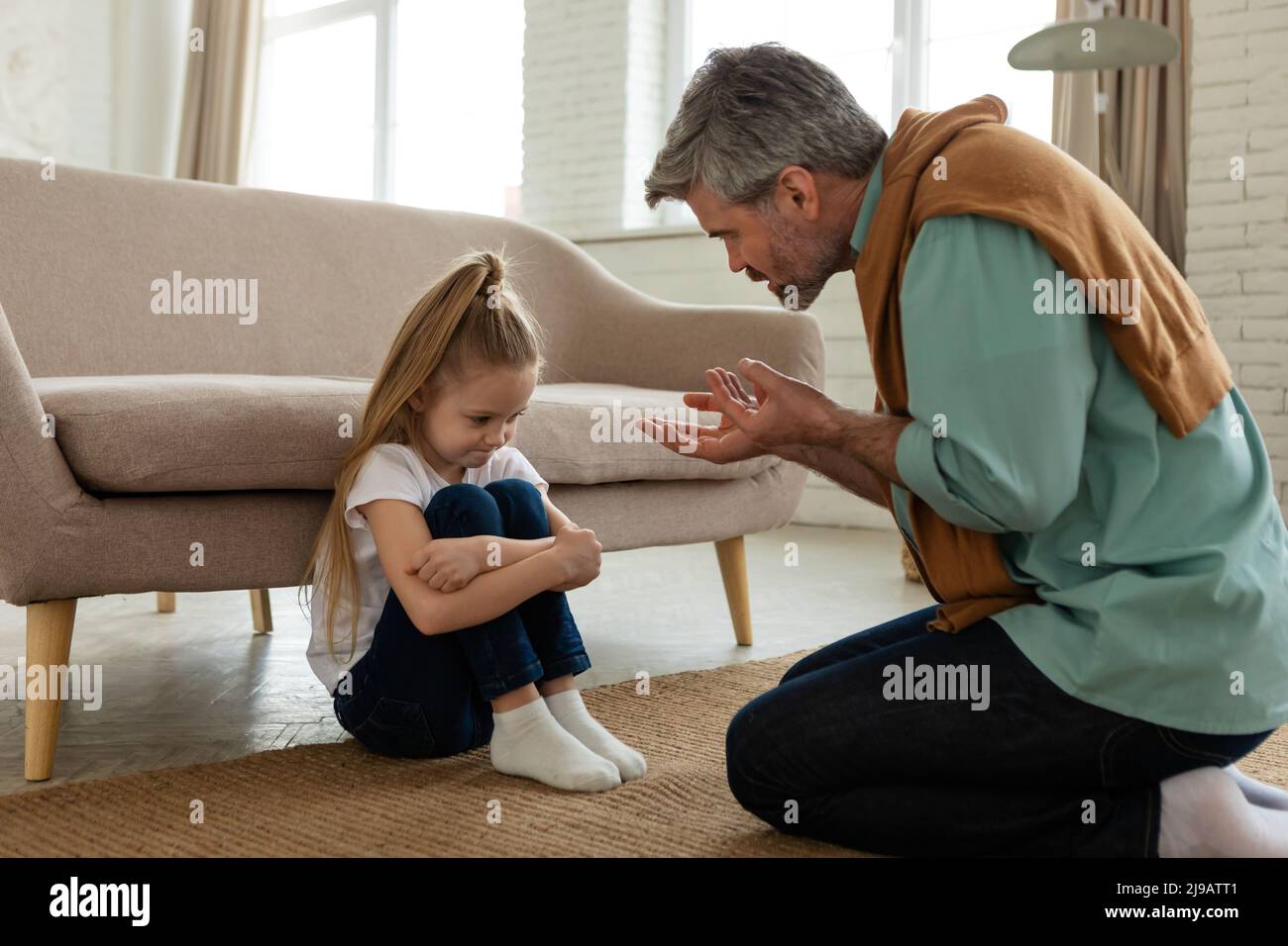 Padre severo che scolding figlia infelice seduta al piano a casa Foto Stock