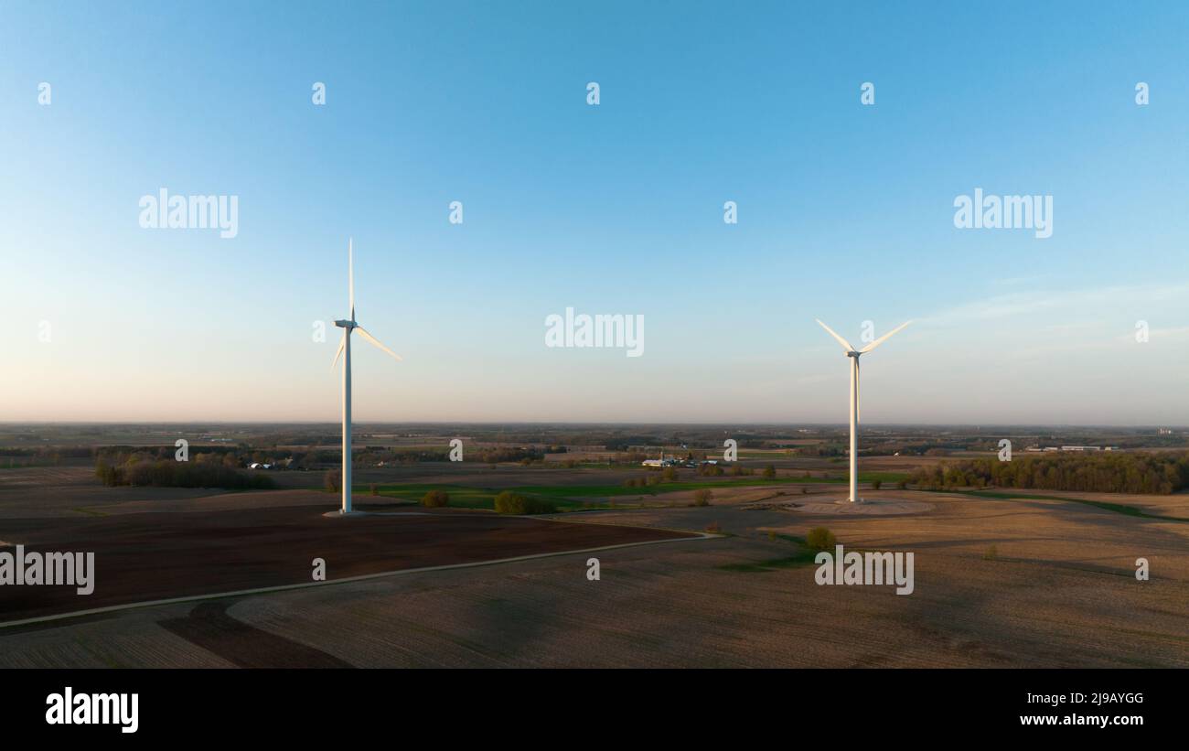 Un paio di turbine eoliche sono viste in un paesaggio rurale, a tarda ora in un pomeriggio di cielo limpido. Foto Stock