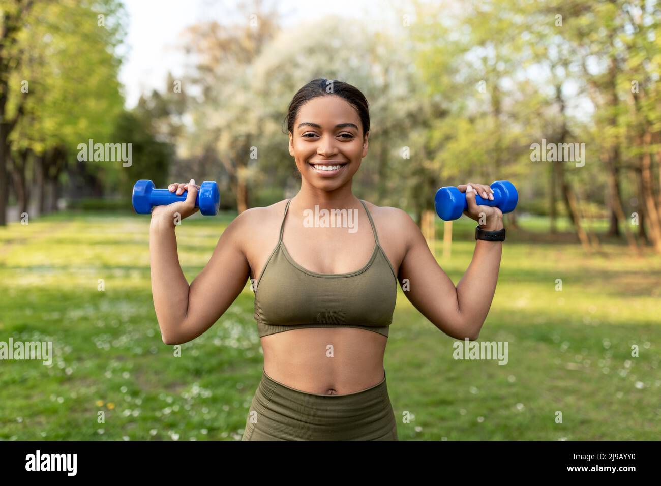 Concetto di allenamento di forza. Fit giovane donna nera facendo esercizi con manubri al parco della città Foto Stock