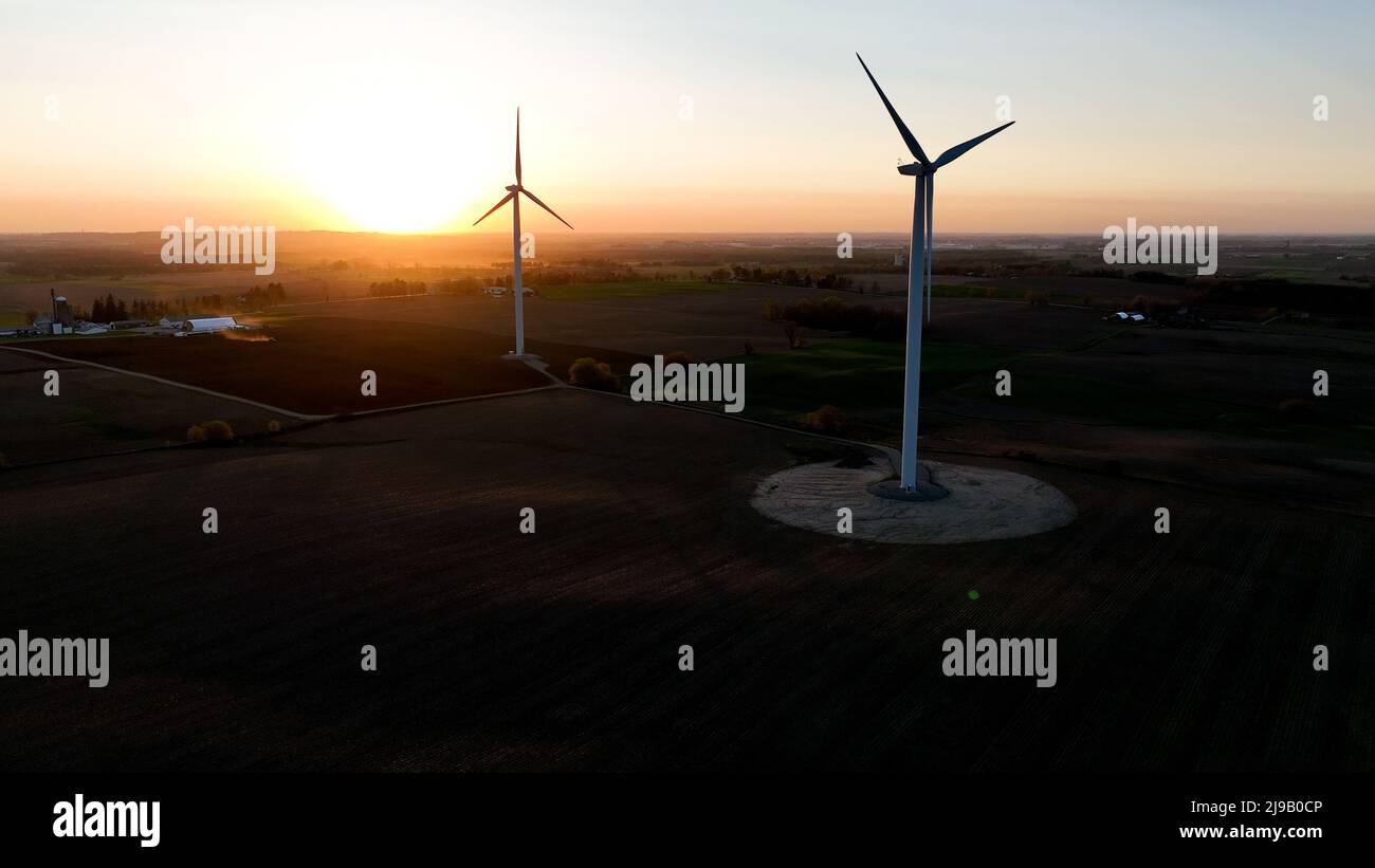 Due turbine eoliche sono raffigurate al tramonto, mentre il paesaggio rurale è catturato mentre il sole crepuscolo splende luminoso. Foto Stock