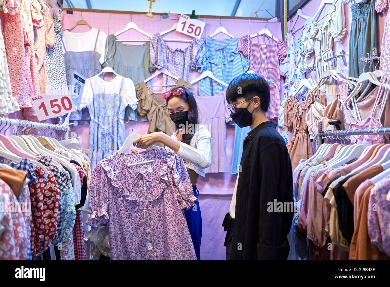 Coppia asiatica non binaria che acquista vestiti in una fiera urbana notturna Foto Stock