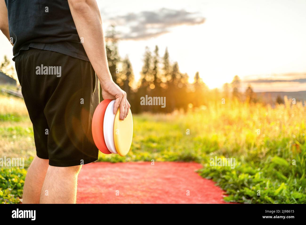 Disco golf in estate al tramonto. Uomo con attrezzatura di frisbee in campo parco. Ragazzo che gioca a discgolf. Giocatore in torneo sportivo all'aperto. Foto Stock