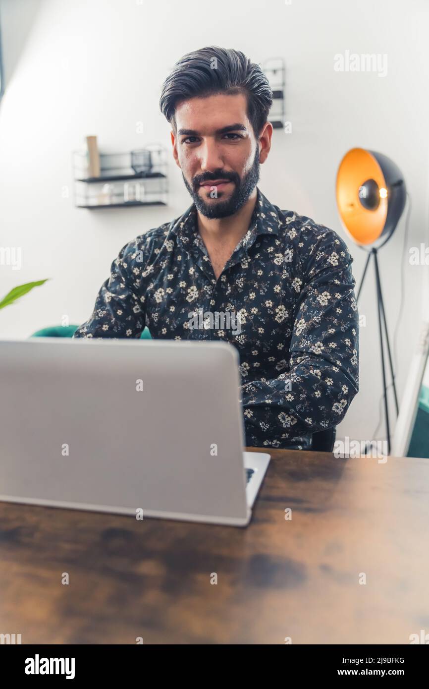 Un uomo di Caucasion che lavora dall'ufficio sul suo laptop e guarda la fotocamera, scatto verticale. Foto di alta qualità Foto Stock