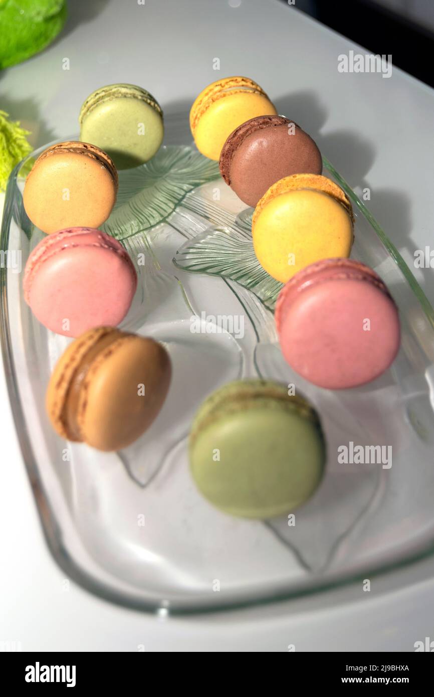 Macaron francesi colorati, biscotti con colori e sapori diversi su un piatto trasparente di vetro. Progettazione di alimenti. Foto Stock
