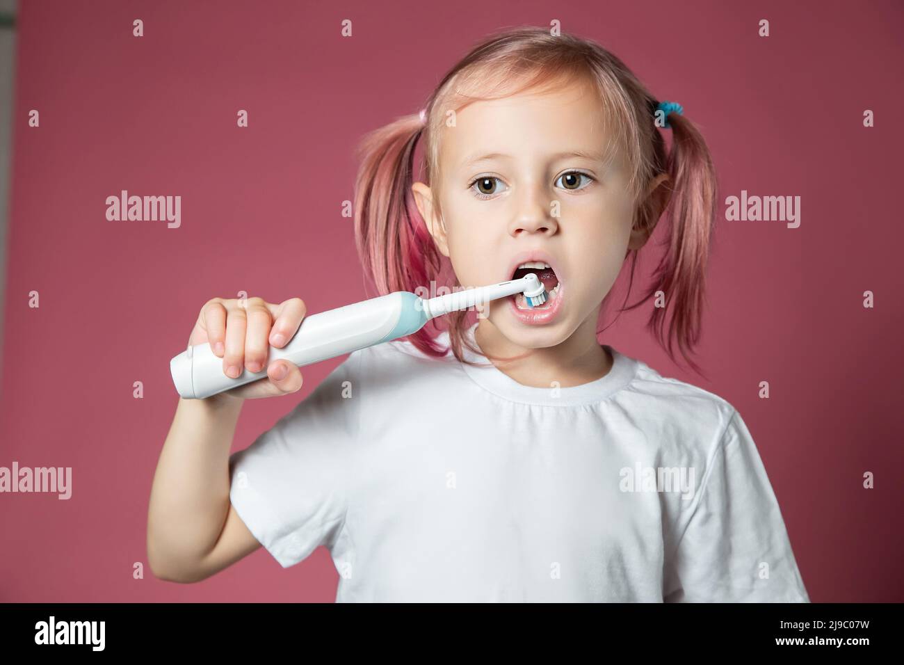 Sorridendo la bambina caucasica pulendo i denti con lo spazzolino elettrico sonico Foto Stock