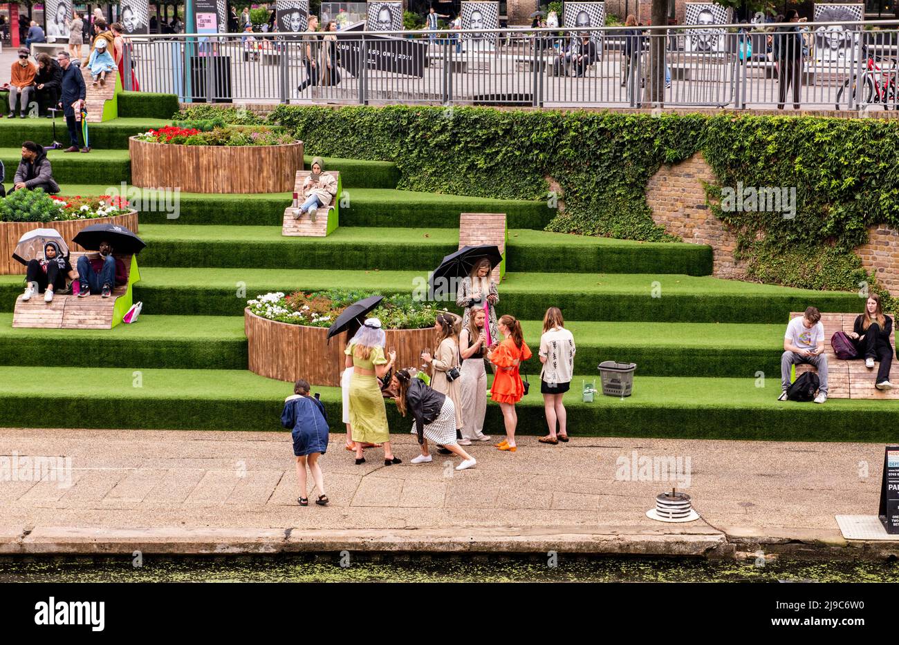 La gente gode il caldo tempo vicino al canale a Granary Square nel centro di Londra mentre le Signore di una festa di gallina si divertono in primo piano e usano gli ombrelloni per ripararsi dal sole. Foto Stock