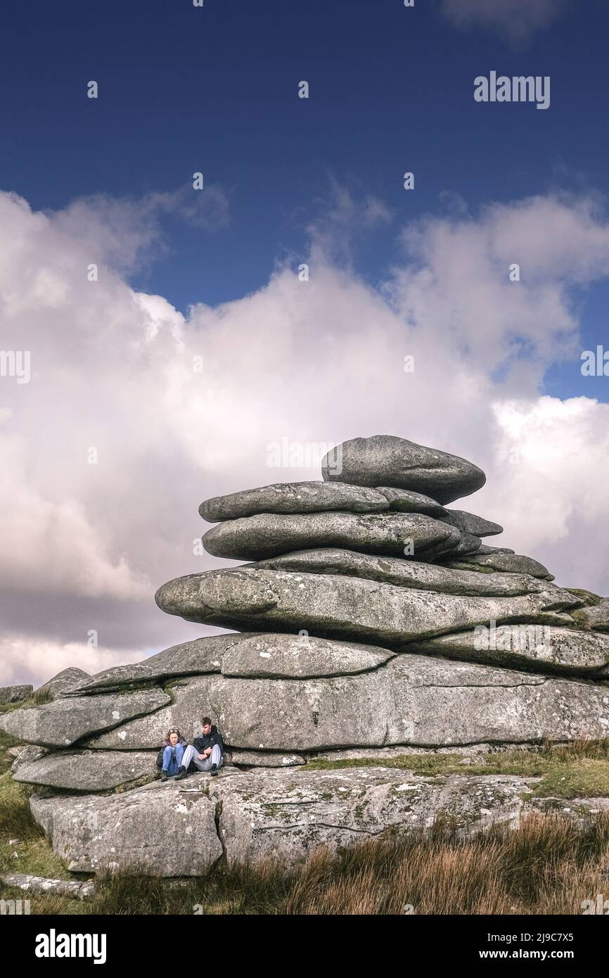 Una giovane coppia che si rilassa sotto un torreggiante scoglio di granito lasciato dall'azione glaciale su Stowes Hill a Bodmin Moor in Cornovaglia. Foto Stock