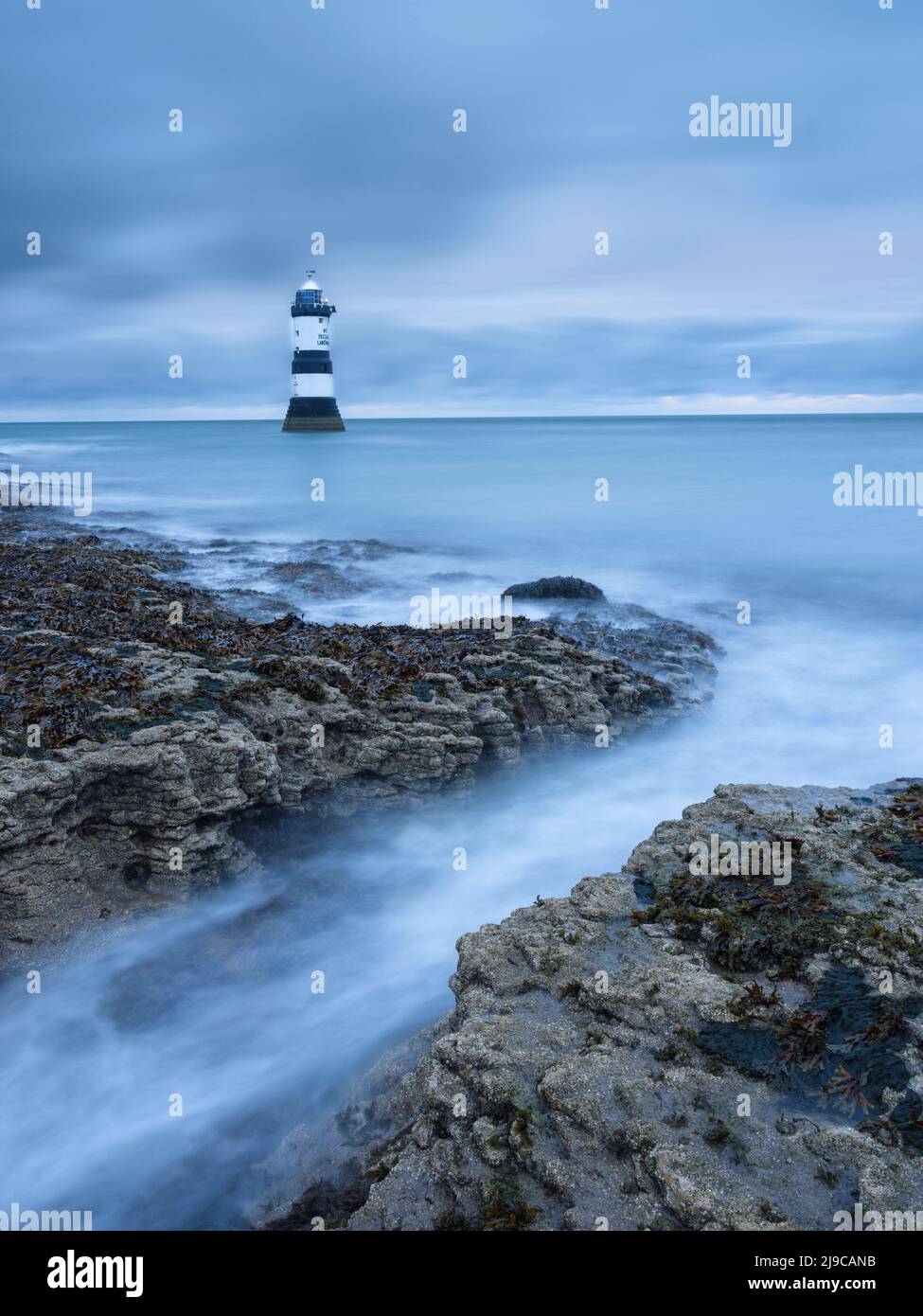 Il faro a Penmon Point su Anglesey con onde che si lavano in primo piano. Foto Stock