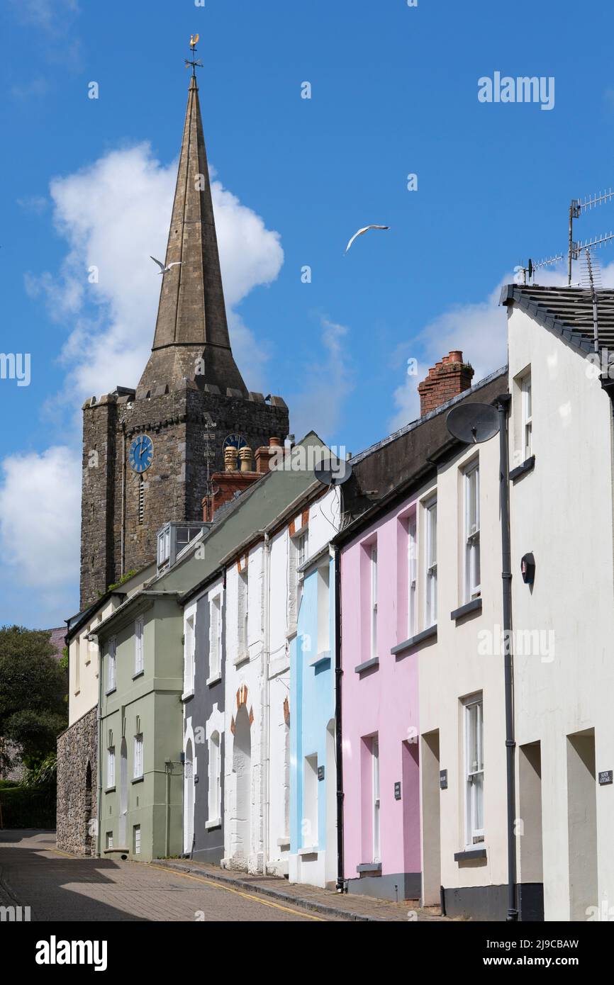 I gabbiani volano dalla torre dell'orologio della chiesa di St Marys e guglia con case color pastello in Cresswell Street alla città portuale di Tenby, Pembrokeshire, Galles Foto Stock