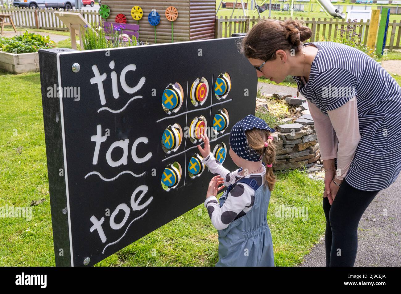 Madre che insegna a sua figlia come giocare i nouights e croci / tic tac punta su una tavola con ruote che girano in Kidwelly Sensory Garden, Kidwelly, Galles Foto Stock