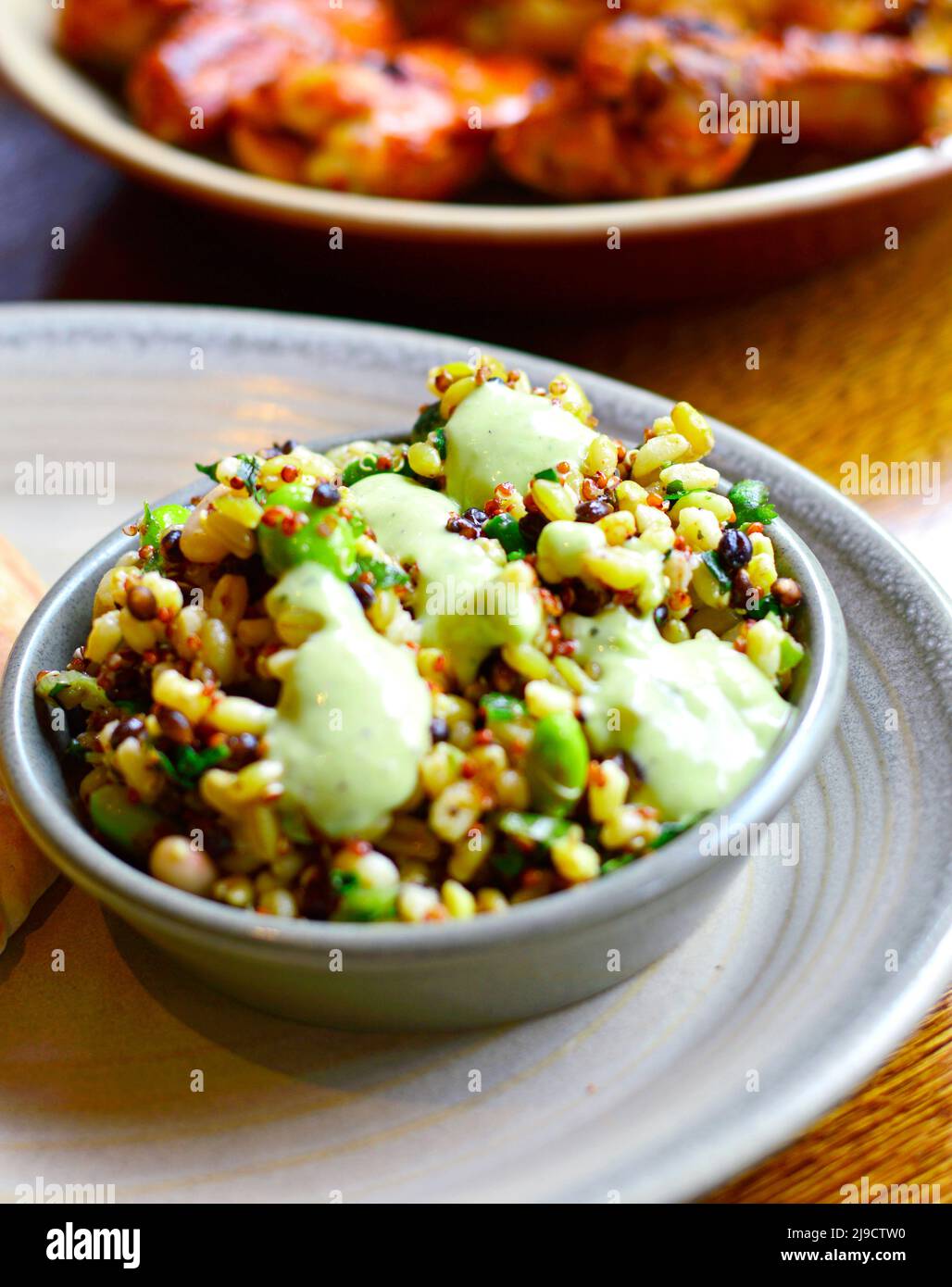 insalata di superfood sana con proteine ricche tra cui quinoa, avocado, fagioli e cereali. Ali di pollo sfocate sullo sfondo. Foto Stock