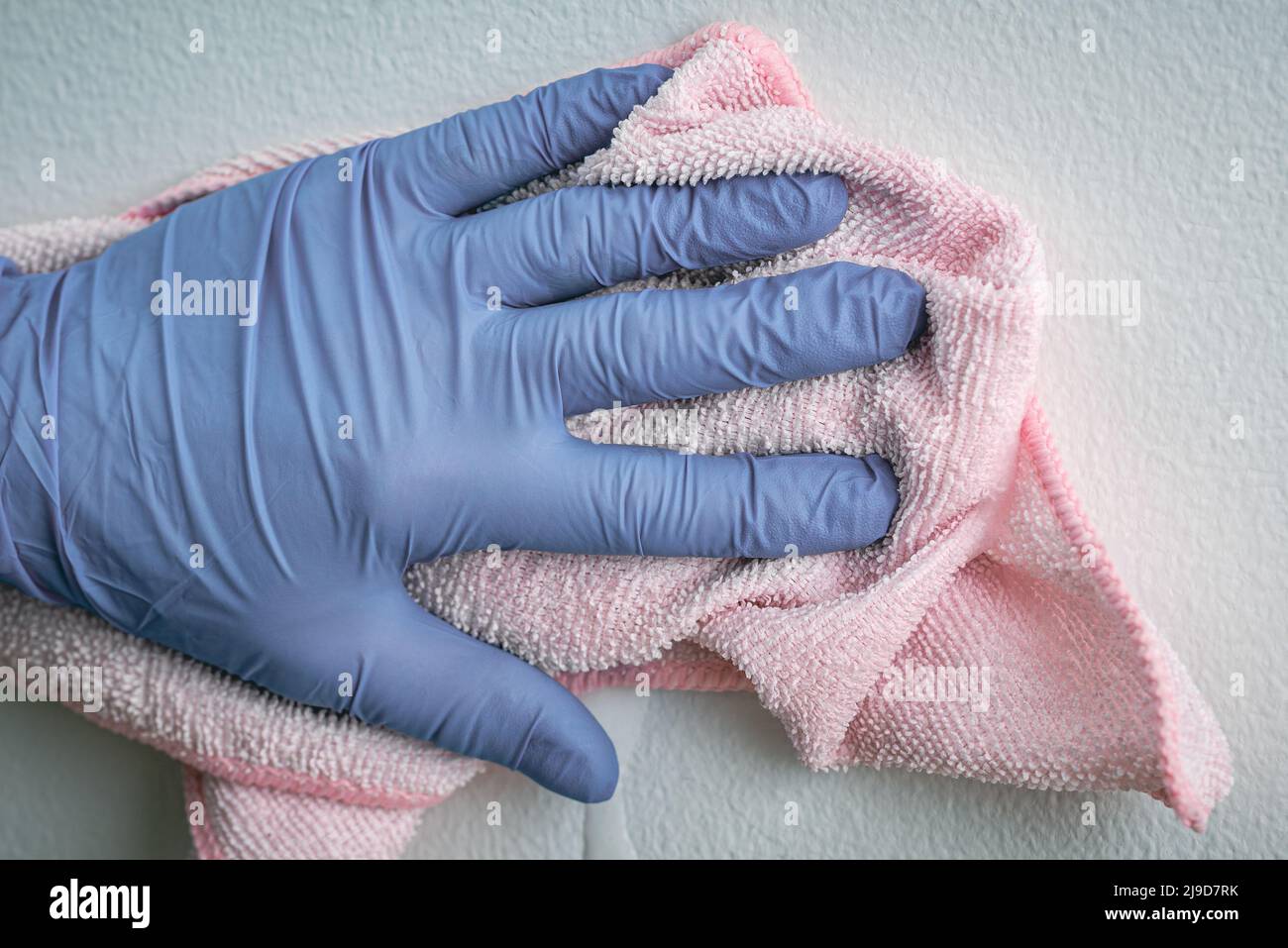 Mano del dipendente in un guanto protettivo in gomma blu con panno in microfibra per rimuovere la parete dalla polvere. La cameriera o la casalinga si preoccupano della casa. Pulizia commerciale Foto Stock